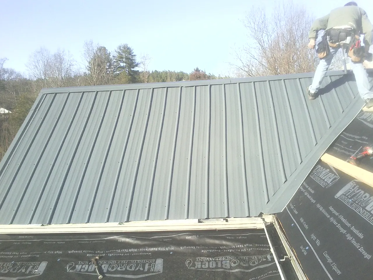 Crew installing dark green standing seam panels over synthetic underlayment in Florahome