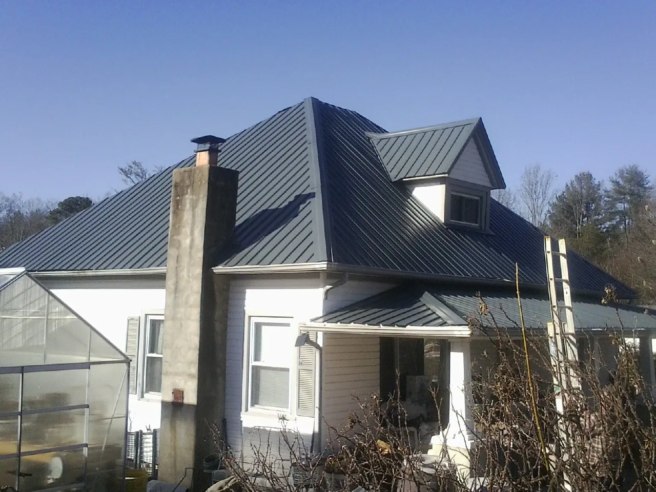 Dark blue standing seam metal roof on a white farmhouse with dormer — Slate & Tile Roof Repair by Roofing Brothers in Florahome