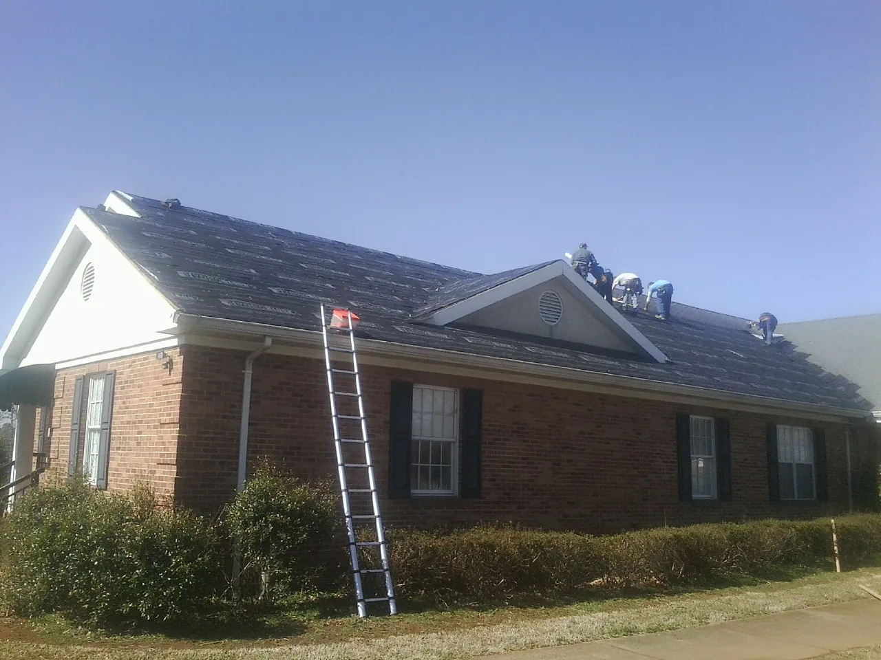 Crew tearing shingles off a brick ranch roof with a ladder set — Metal Roof Repair work by our crew in Florahome