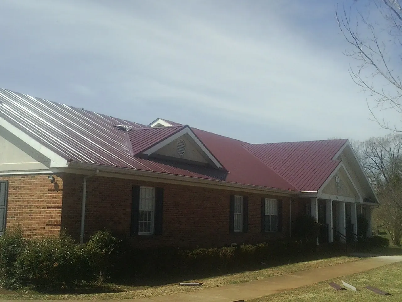 Red metal roof with gabled entries on a long brick building, from a Hail Damage Roof Repair job in Florahome