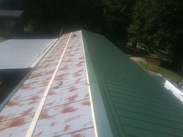 Old rusted panels beside newly installed green metal roofing — Wind Damage Roof Repair by Roofing Brothers in Florahome