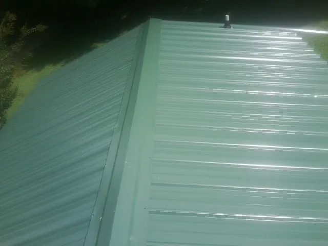 New green metal panels meeting at the ridge of a roof — Flat Roof Repair work by our crew in Florahome