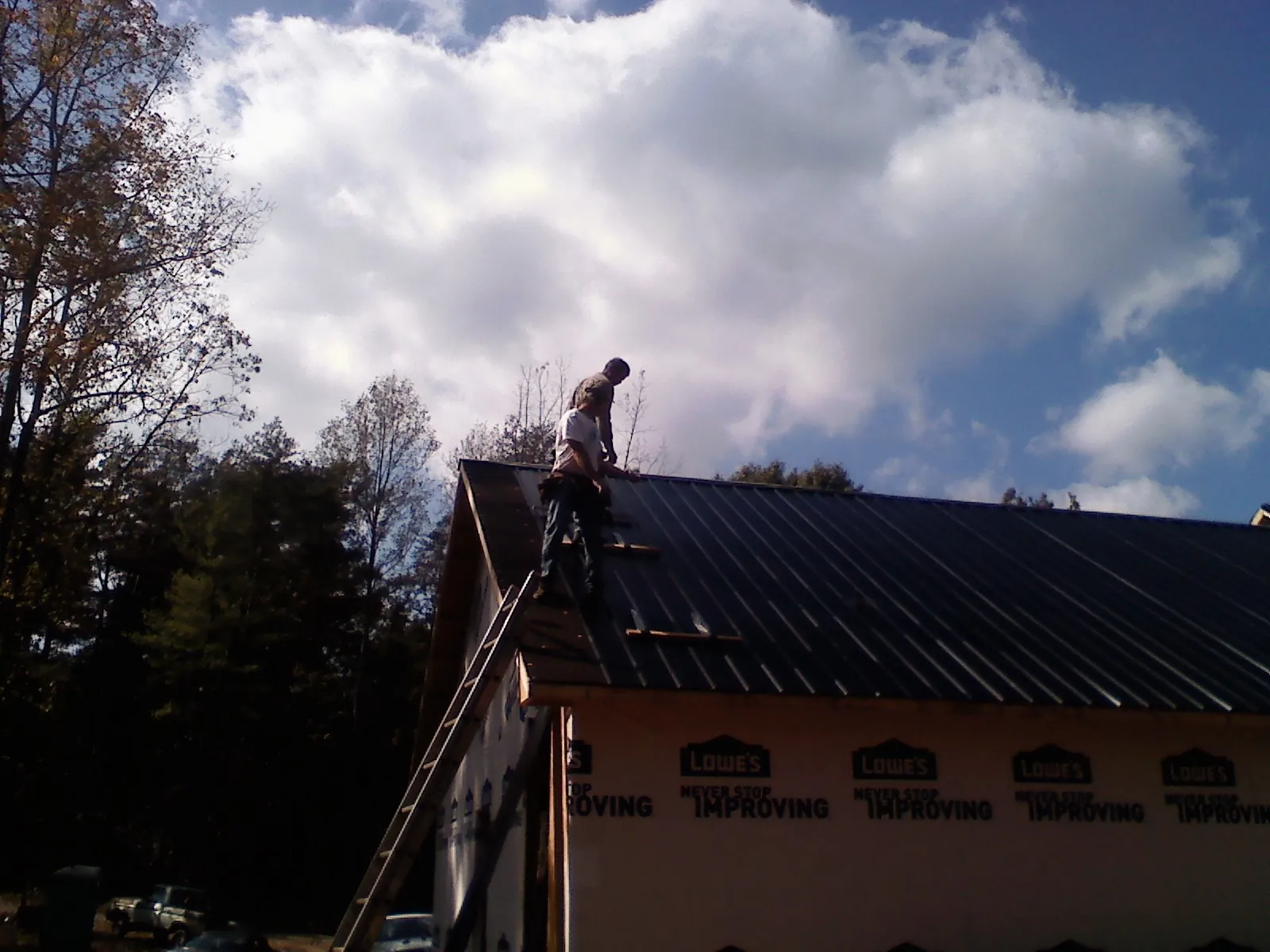 Roofer fastening dark metal panels high against a cloudy sky, from a Roof Inspection job in Florahome