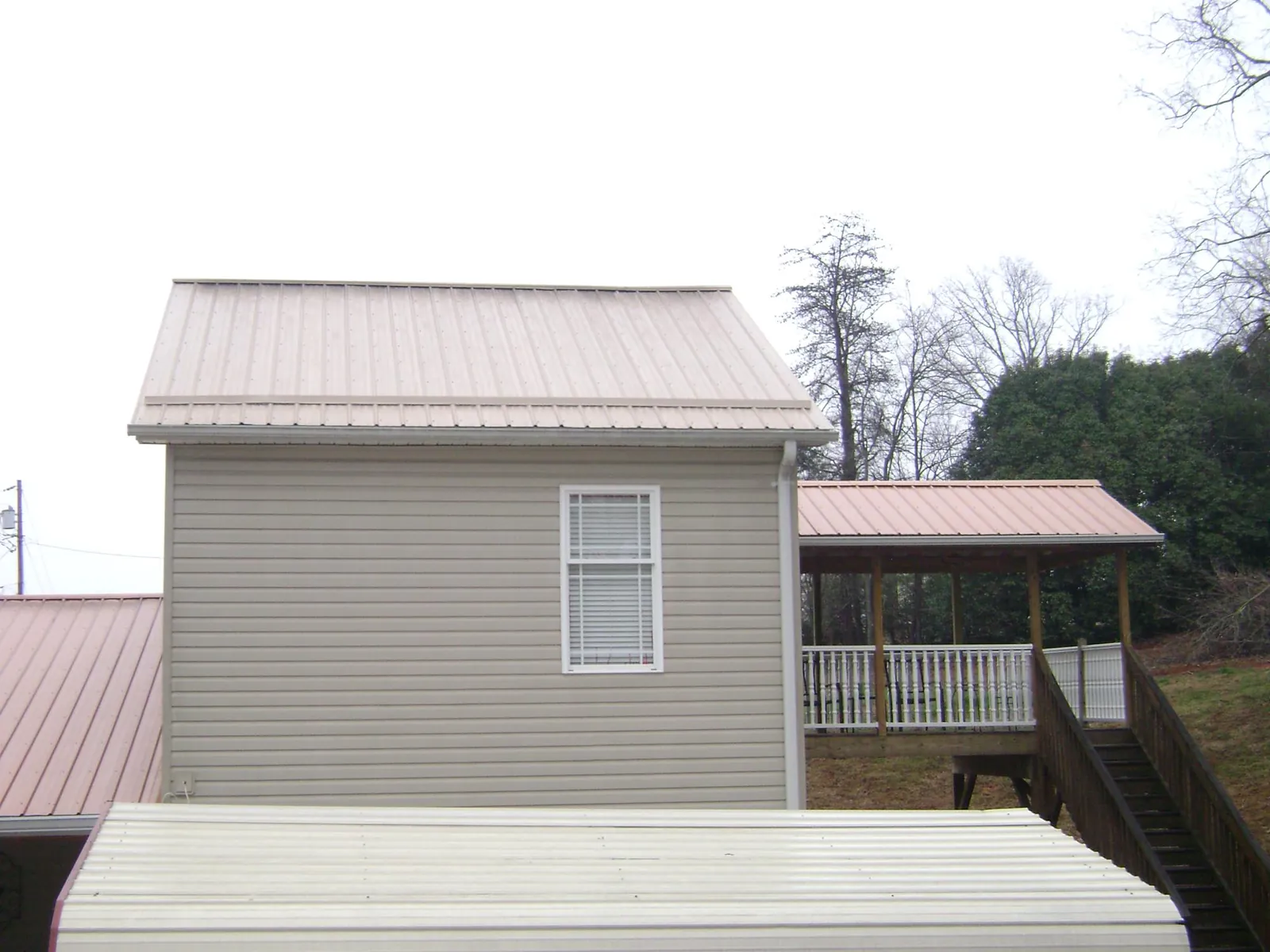 Tan metal roofs on a two story addition and attached porch, from a Roof Replacement job in Florahome